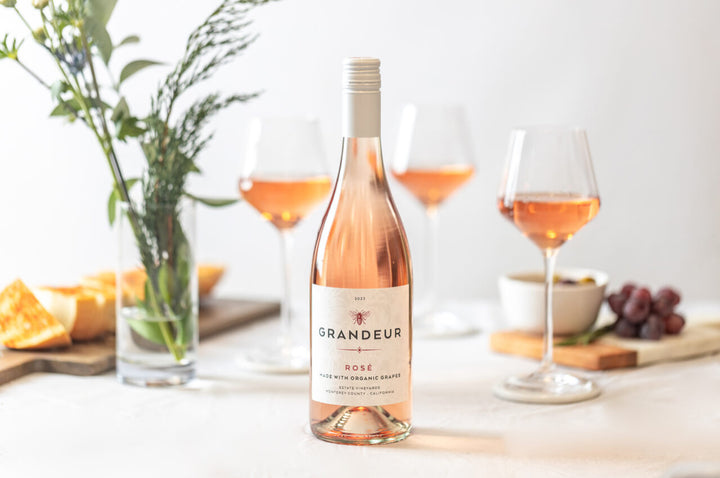 A bottle of Grandeur Rose sitting on top of a table with glasses in the background